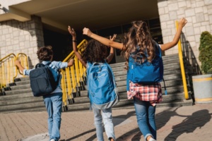 Group of happy multiracial schoolmates elementary middle school kids pupils walking to school together running hurrying to the building for classes lessons.